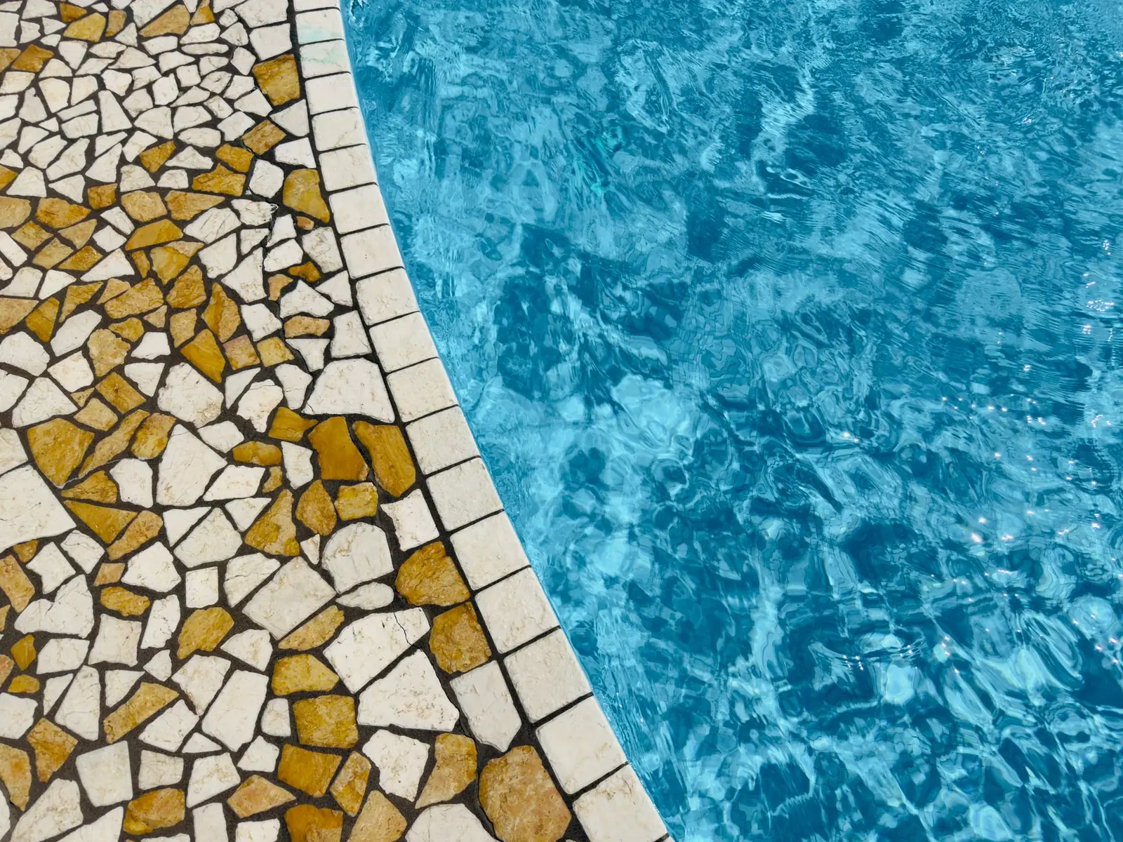 Gold and white mosaic tile band at the waterline of a swimming pool